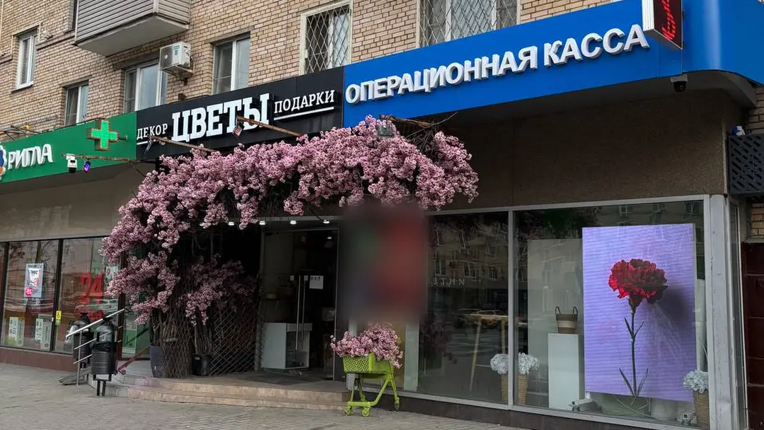 Синяя вывеска «Операционная касса» над витриной, слева — цветочный магазин